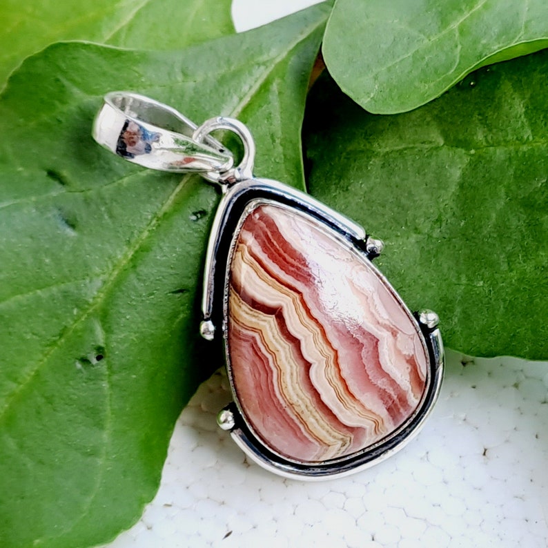 May include: A silver pendant with a teardrop-shaped pink and white agate stone. The stone has a swirling pattern of pink, white, and brown.