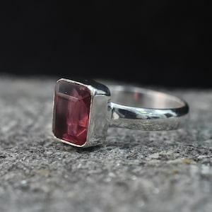 Pode incluir: Um anel de prata com uma grande pedra preciosa retangular, facetada e rosa.