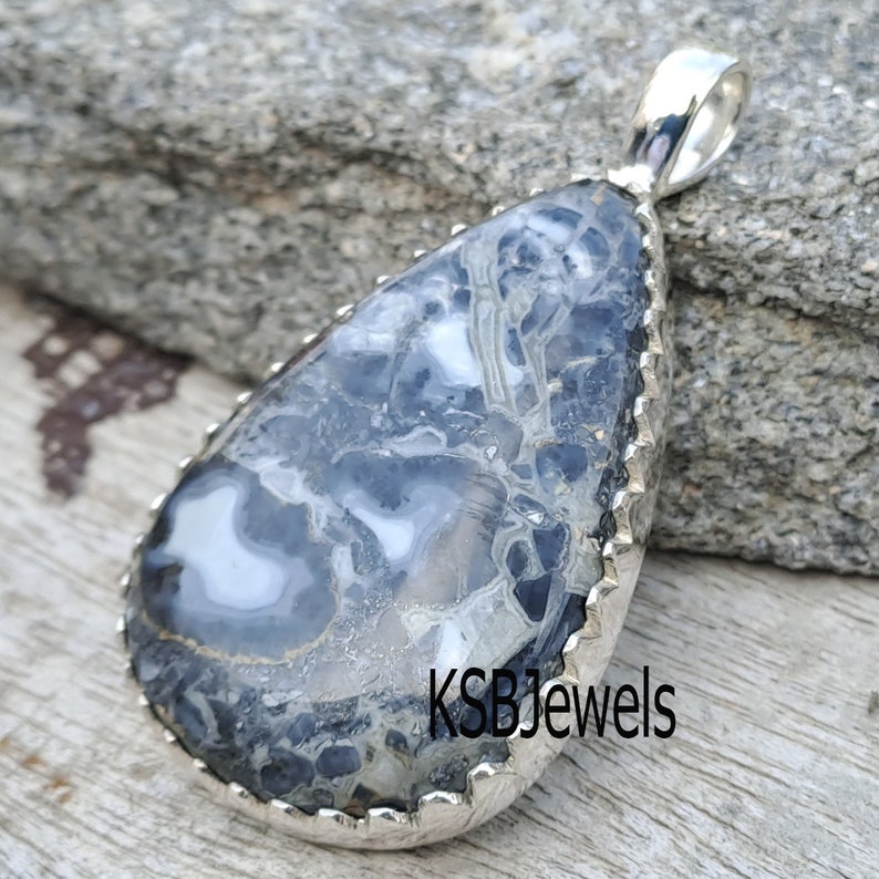 May include: A silver pendant with a teardrop-shaped, black and white agate stone. The stone has a unique, swirling pattern. The pendant has a scalloped edge and a silver bail.