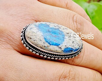 May include: A silver ring with a large oval blue and white gemstone set in a silver bezel. The ring is on a person's finger.