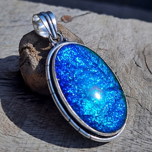 May include: A silver oval pendant with a blue and green dichroic glass inlay. The glass has a sparkly, iridescent finish.