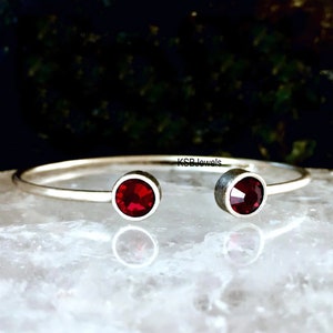 Puede incluir: Un brazalete de plata con dos acentos de cristal rojo. KSBJewels está impreso en el brazalete.