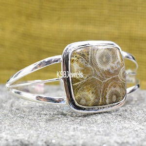 Può includere: Un braccialetto d'argento con una pietra quadrata di corallo fossilizzato di colore marrone chiaro al centro. La pietra presenta un motivo unico di cerchi bianchi.