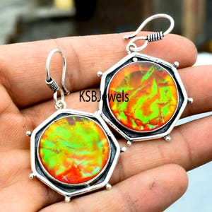 Puede incluir: Un par de pendientes de plata con engastes octogonales que presentan cabujones de piedras preciosas iridiscentes verdes, naranjas y rojas. KSBJewels está impreso en la imagen.