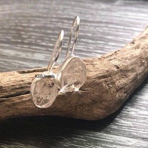 Könnte beinhalten: Ein Paar Ohrringe aus klaren, facettierten Edelsteinen mit silberfarbenen Haken. Die Ohrringe werden auf einem Stück Treibholz präsentiert. Der Text "KSBJewels" ist im Bild zu sehen.