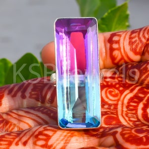 May include: A silver ring featuring a large, rectangular, iridescent gemstone. The gemstone is a gradient of purple, pink, and blue.