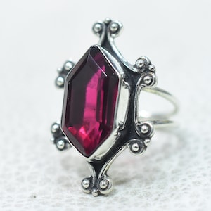May include: A silver ring with a large, faceted, dark pink gemstone set in a decorative, ornate design.