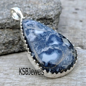 May include: A silver pendant with a teardrop-shaped blue and white agate stone. The stone has a swirling pattern and is set in a silver bezel with a scalloped edge. KSBJewels is printed on the bottom of the image.