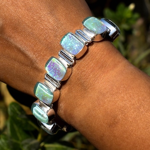May include: A silver bracelet with iridescent blue and green opal stones. The bracelet has a link style with a clasp closure.