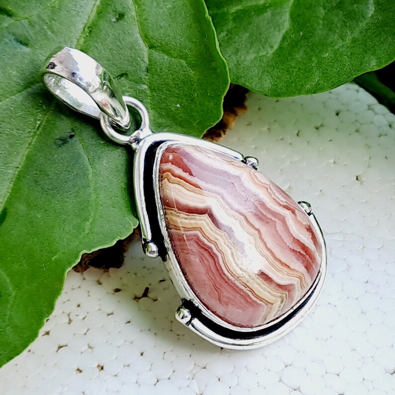 May include: A silver pendant with a pink and white agate stone. The stone has a swirling pattern of pink, white, and brown.