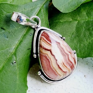 May include: A silver pendant with a teardrop-shaped, pink, white, and brown agate stone. The stone has a swirling pattern.