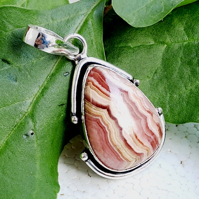May include: A silver pendant with a teardrop-shaped, pink, white, and brown agate stone. The stone has a swirling pattern.