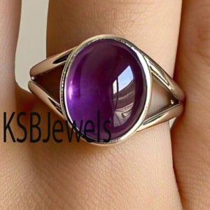 May include: A silver ring featuring a large, oval-shaped, purple gemstone. The ring has a split band design.