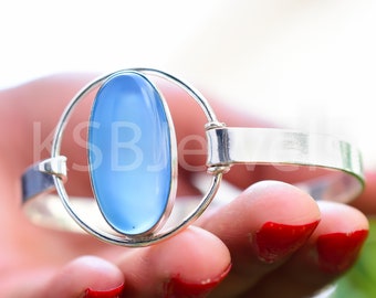 May include: A silver bracelet with a light blue oval gemstone set in a circular frame.