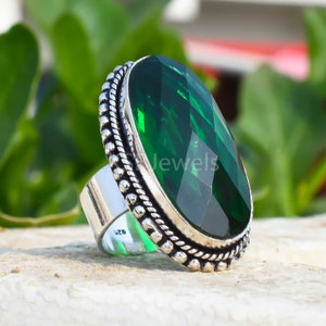 May include: A silver ring featuring a large, oval-shaped green gemstone set in an ornate silver bezel. The ring has a textured band and a beaded edge.