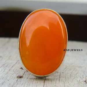 Può includere: Un anello d'argento con una grande pietra preziosa arancione di forma ovale. L'anello è incastonato in una semplice fascia d'argento.
