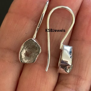 Könnte beinhalten: Ein Paar silberne Ohrringe mit rauen, grauen Diamanten. Die Ohrringe haben ein schlichtes, hakenförmiges Design.