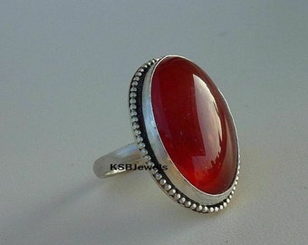 May include: A silver ring with a large, oval-shaped, red carnelian gemstone. The ring has a beaded border around the stone.