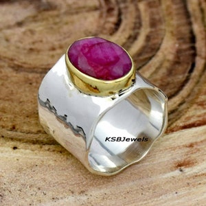 Może przedstawiać: Srebrny pierścionek z fakturą młotkową i złotym oprawą. Pierścionek ma duży, owalny rubin.