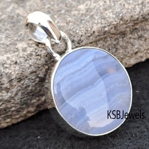 May include: A silver pendant featuring a round blue agate gemstone with white and gray banding. The pendant has a simple bail for attaching to a chain. KSBJewels is printed on the bottom right corner of the image.