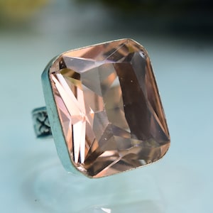 May include: A silver ring with a large, faceted, light pink gemstone. The gemstone is set in a square shape and has a high polish.