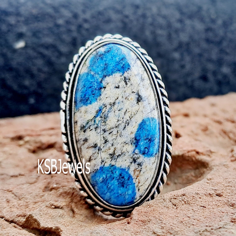 May include: A silver ring featuring a blue and white oval gemstone. The ring has a rope-like design around the edge of the setting.