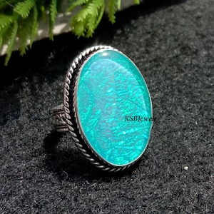 Puede incluir: Un anillo de plata con una gran piedra ovalada de ópalo azul turquesa engastada en un engaste de plata. El anillo tiene un diseño de cuerda alrededor del engaste.