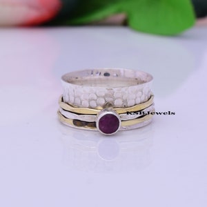 May include: A silver and gold spinning ring with a purple gemstone. The ring has a hammered texture and is made of three bands.
