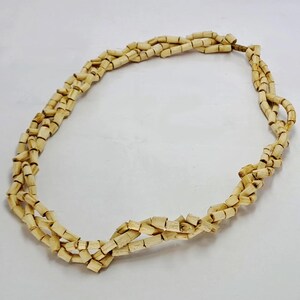 Pu&ograve; includere: Una collana realizzata con perline di legno di colore beige naturale. Le perline sono piccole e rettangolari e sono infilate insieme in un semplice motivo. La collana &egrave; lunga circa 45 cm.