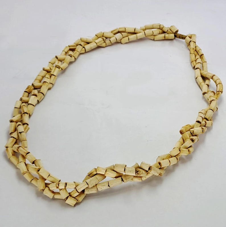 Pu&ograve; includere: Una collana realizzata con perline di legno di colore beige naturale. Le perline sono piccole e rettangolari e sono infilate insieme in un semplice motivo. La collana &egrave; lunga circa 45 cm.