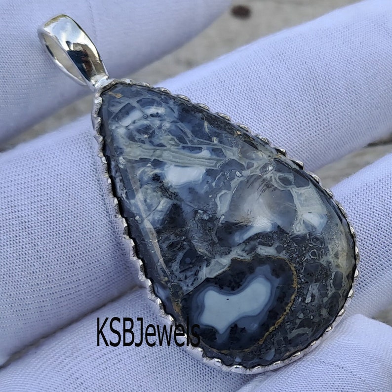 May include: A silver pendant featuring a teardrop-shaped, black and white agate stone with a silver bezel. The stone has a unique, swirling pattern.