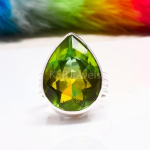 Pode incluir: Um anel de prata com uma grande gema verde em forma de pêra. A gema tem um corte facetado e está engastada em uma banda de prata.