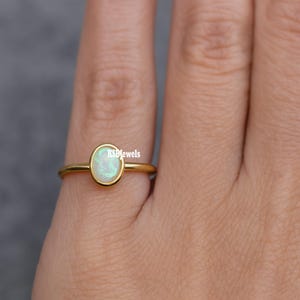 Könnte beinhalten: Ein goldener Ring mit einem ovalen, schillernden Opal-Edelstein. Der Opal ist in einer Lünettenfassung gefasst. Der Ring befindet sich an einem Finger.