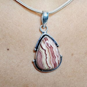 May include: A silver pendant with a teardrop-shaped pink and white agate stone. The stone has a swirling pattern of pink, white, and brown.