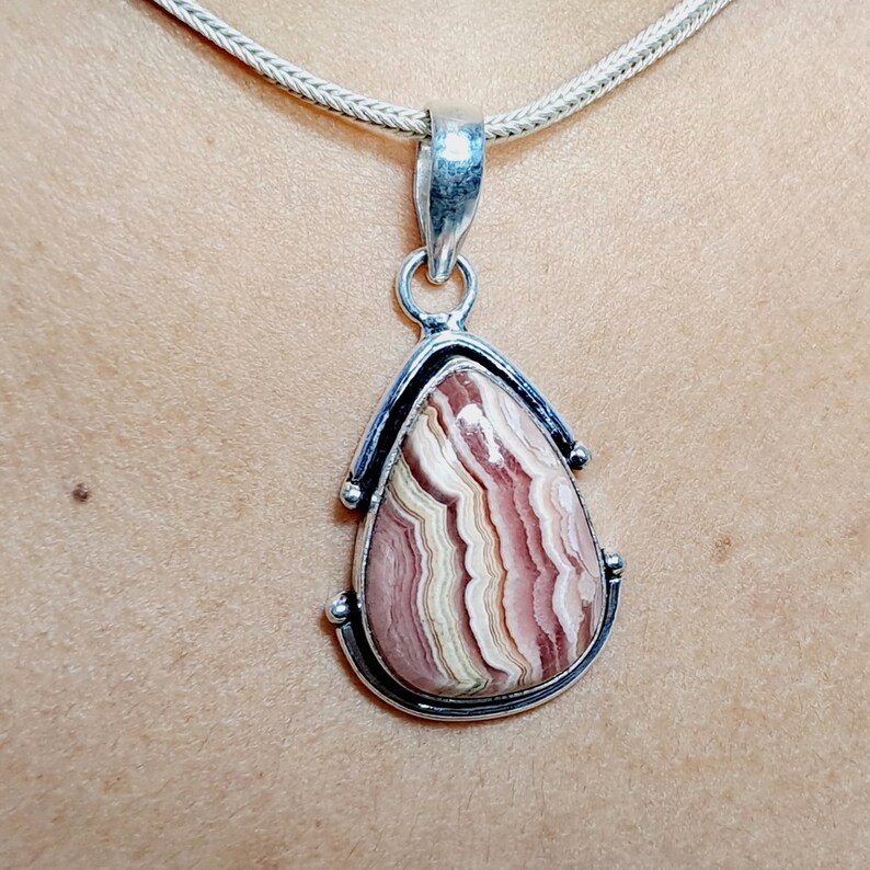 May include: A silver pendant with a teardrop-shaped pink and white agate stone. The stone has a swirling pattern of pink, white, and brown.