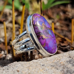 May include: A silver ring featuring a purple and gold oval gemstone. The ring has a triple band design.
