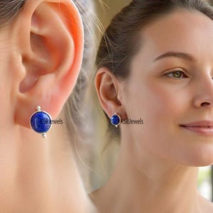 Könnte beinhalten: Ein Paar silberne Ohrstecker mit einem runden blauen Edelstein. Die Ohrringe sind an einem Ohrmodell zu sehen.