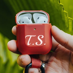 May include: Red Airpods case with a white monogram "T.S." and a red lanyard.