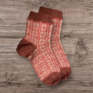 May include: A pair of knitted socks with a geometric pattern in shades of pink and beige. The socks have a brown cuff.
