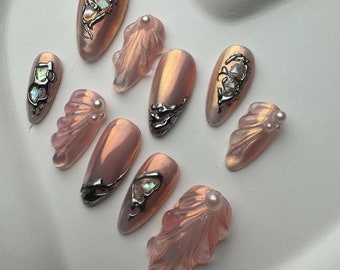 May include: Set of ten pink and white press-on nails with pearl accents and silver detailing. The nails are in various shapes and sizes, including oval, square, and almond.