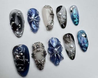 May include: Ten different nail designs featuring blue, white, and silver accents. Some designs include flowers, crosses, and pearls.