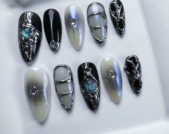 May include: Ten different nail designs featuring a variety of colors, shapes, and textures. Some nails have a black base with silver accents, while others have a white base with silver accents. Some nails have a blue gemstone accent.