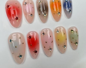 May include: Ten different colored fake nails with a gradient effect and gold glitter. Each nail has a clear base with a different color gradient and gold glitter.