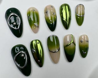 Puede incluir: Diez puntas de uñas verdes y plateadas con diferentes diseños. Algunas tienen brillo, otras tienen un acabado metálico y otras tienen un efecto degradado.