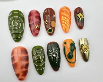 Könnte beinhalten: Satz mit zehn falschen Nägeln mit verschiedenen Designs. Die Nägel sind mandelförmig und in den Farben Grün, Orange, Braun und Rot gehalten. Einige Nägel haben goldene Akzente und Verzierungen.