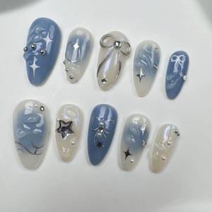 May include: Ten blue and white false nails with different designs. Some nails feature silver stars, bows, and swirls.