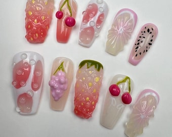 May include: Set of ten pink and white fake nails with fruit designs. The designs include strawberries, cherries, grapes, watermelon, lemons, and a bubble design.