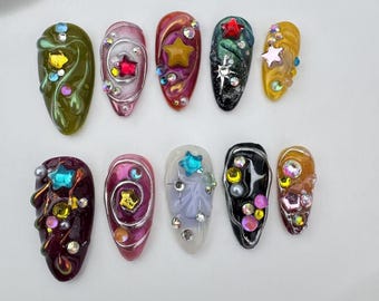 Può includere: Dodici diversi design di nail art con vari colori, forme e accenti di glitter. Ogni design è un pezzo unico e intricato di nail art.