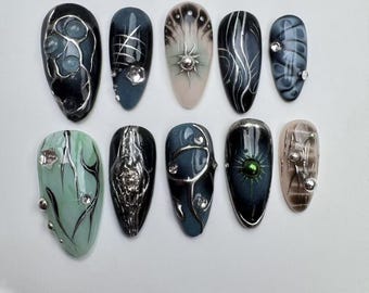 Puede incluir: Diez uñas postizas largas en forma de almendra con diferentes diseños. Las uñas están pintadas en tonos de negro, blanco y verde con acentos plateados y blancos. Algunas uñas tienen pequeños diamantes de imitación.