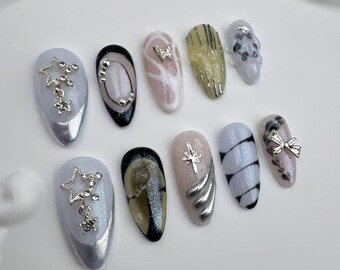 May include: Set of ten false nails with various designs. Some nails feature silver stars, a butterfly, and a bow. Others have a marble effect, a glitter finish, and a silver stripe.
